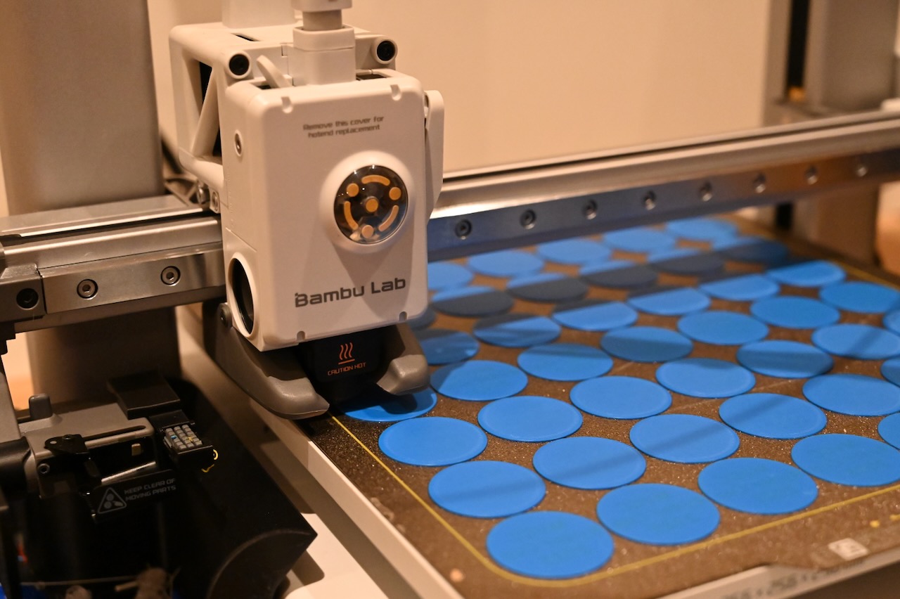 A 3D printer printing blue flat golf tees